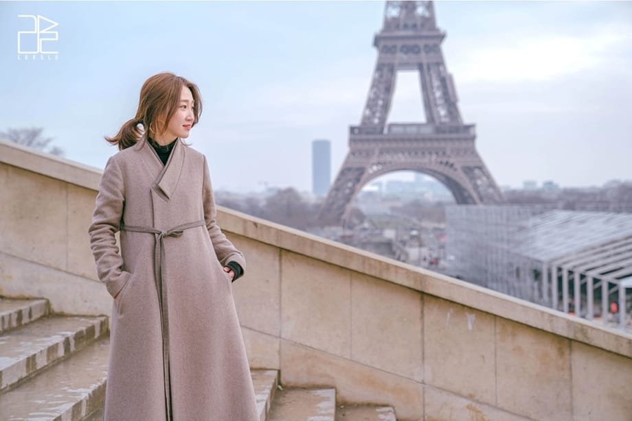 Frau, die in der Ferne auf einer Treppe vor dem Eiffelturm steht
