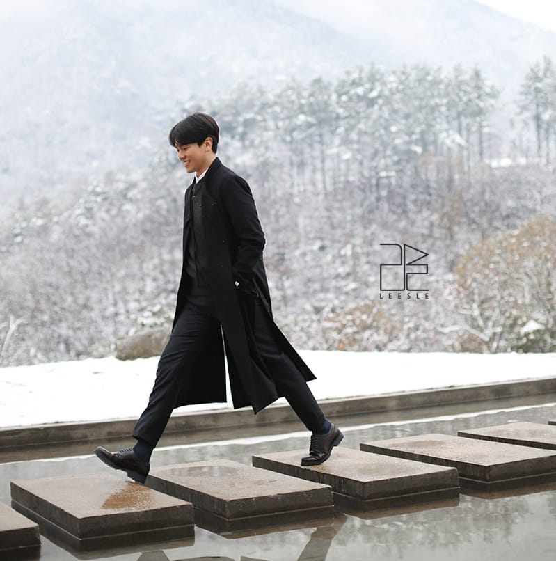 A man wearing a black winter coat crossing a stepping stone