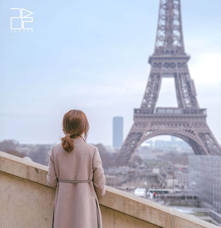 Frau, die in der Ferne auf einer Treppe vor dem Eiffelturm steht, Rückansicht