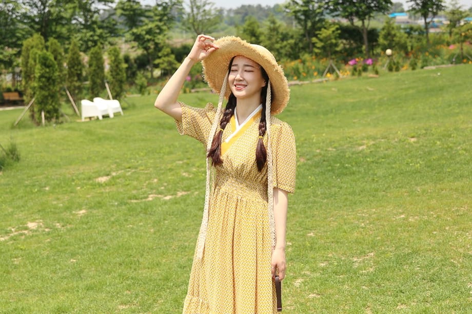 Une femme portant un chapeau jaune et une robe, sur fond de pelouse verte
